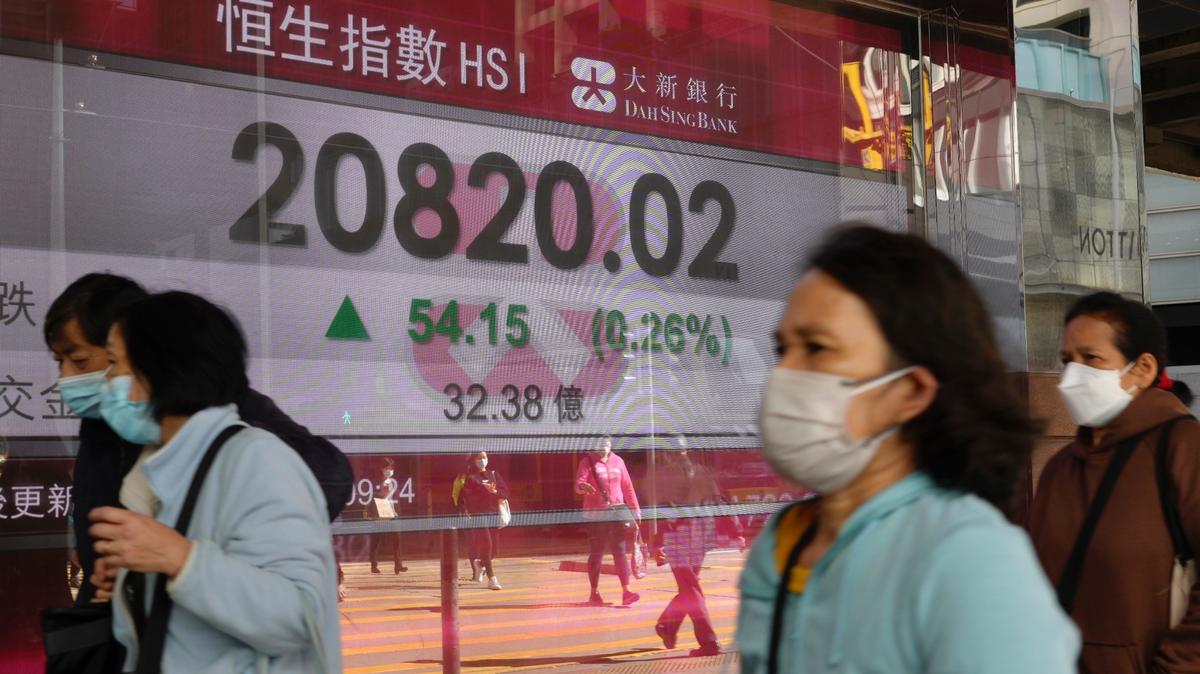 Varias personas caminan frente al tablero electrónico de un banco que muestra el índice de acciones de Hong Kong en la Bolsa de Valores de Hong Kong el miércoles 9 de marzo de 2022. (Foto AP/Vincent Yu)
