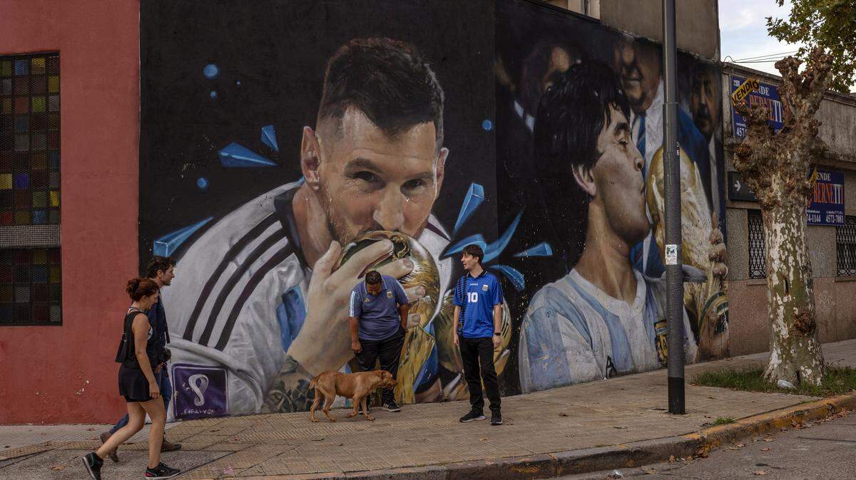 Soccer fans Jose Serio, center, and Rodrigo Diez, right, hang out in front of one of the many murals depicting Argentine soccer legends Lionel Messi and Diego Maradona in Buenos Aires on April 14. Dynamic ticket pricing has made this year’s World Cup tournament the most expensive in history, pushing Argentine fans to extremes. 