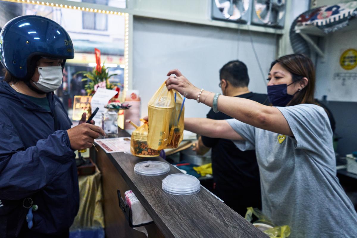 Yeh Pi-chiu, who manages a rice vermicelli noodle shop near the Xizhou Public Market, hands a delivery driver an order in Taipei, Taiwan on April 8, 2026. Yeh started charging customers one Taiwan dollar -- roughly 3 cents -- for every plastic bag their order required (An Rong Xu/The New York Times)
