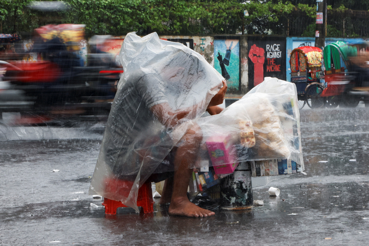 A hawker who sells cigarettes and snacks covers himself with polythene during torrential rain in Dhaka, Bangladesh, July 7, 2026. REUTERS/Mohammad Ponir Hossain