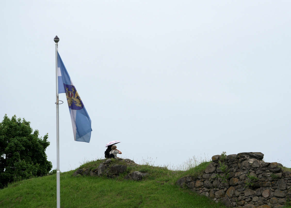 People sit on a hilltop next to the Latgalian regional flag in Rezekne, Latvia, June 8, 2026. REUTERS/Janis Laizans