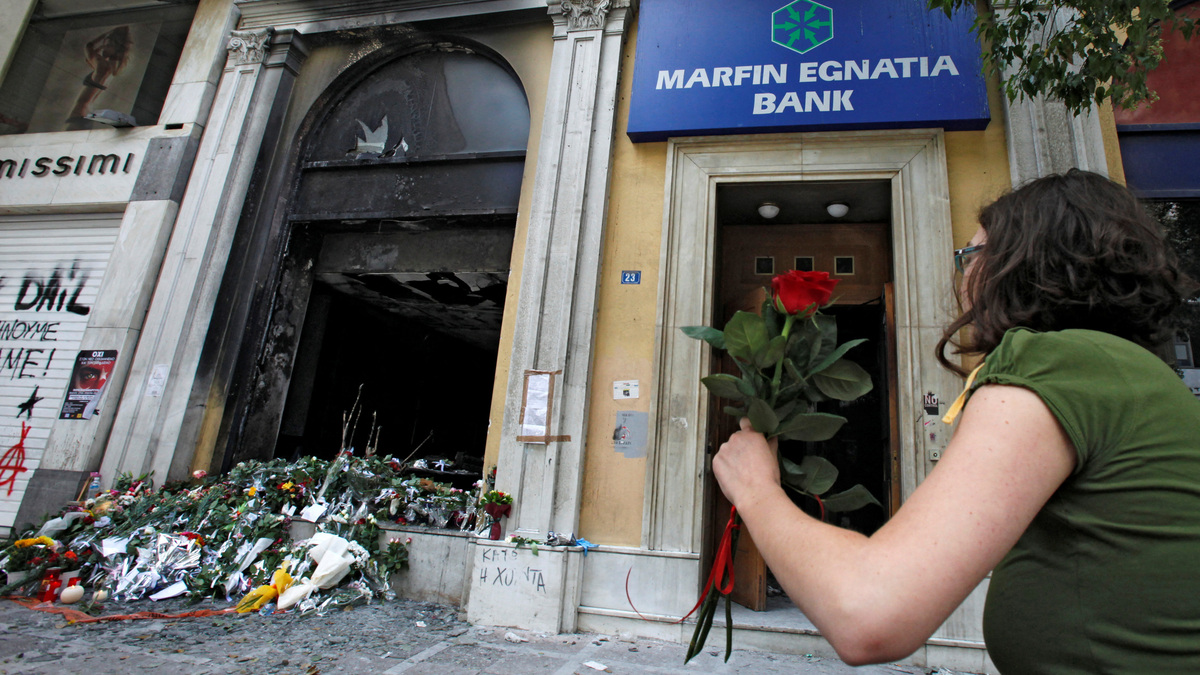 FILE PHOTO: A woman arrives to place a flower outside a burned-out bank, May 6, 2010 , which was set on fire during violent demonstrations in Athens a day earlier. REUTERS/Pascal Rossignol/File Photo