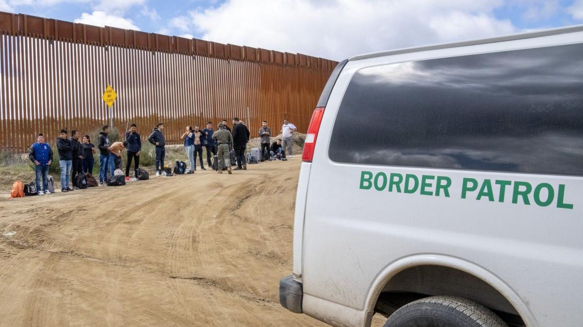 Migrants wait to surrender to the U.S. Border Patrol after crossing the border wall from Mexico near Campo, Calif., in 2024. Border Patrol Chief Mike Banks resigned Thursday. File Photo by Pat Benic/UPI