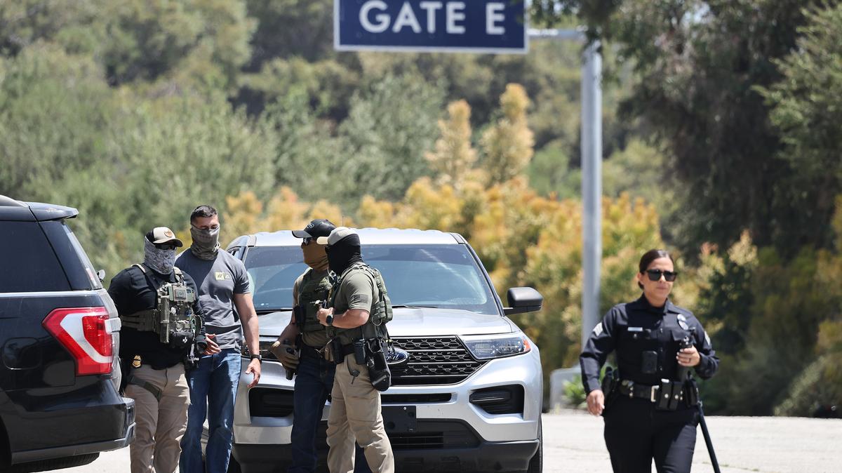 A Los Angeles Police Department officer walks near masked federal agents staged outside a gate of Dodger Stadium on June 19, 2025, in Los Angeles. (Mario Tama/Getty Images/TNS)