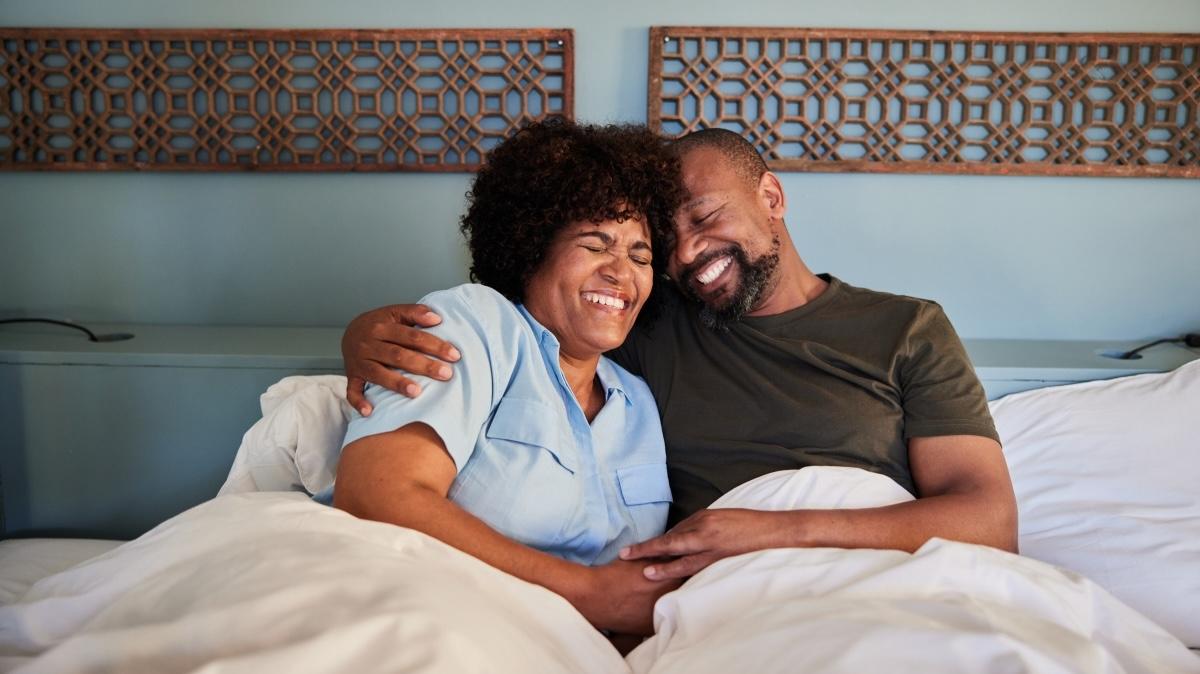 Loving mature couple laughing together while lying in their bed at home after waking up in the morning