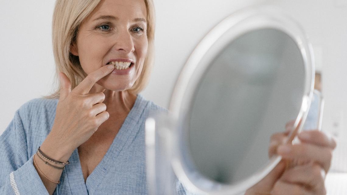 Mature woman looking in beauty mirror in bathroom checking her teeth