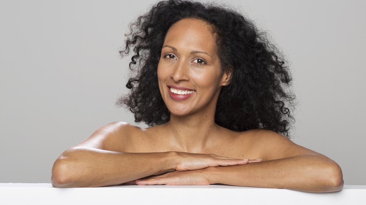 Portrait of smiling mid adult woman leaning on polystyrene while standing against grey background.