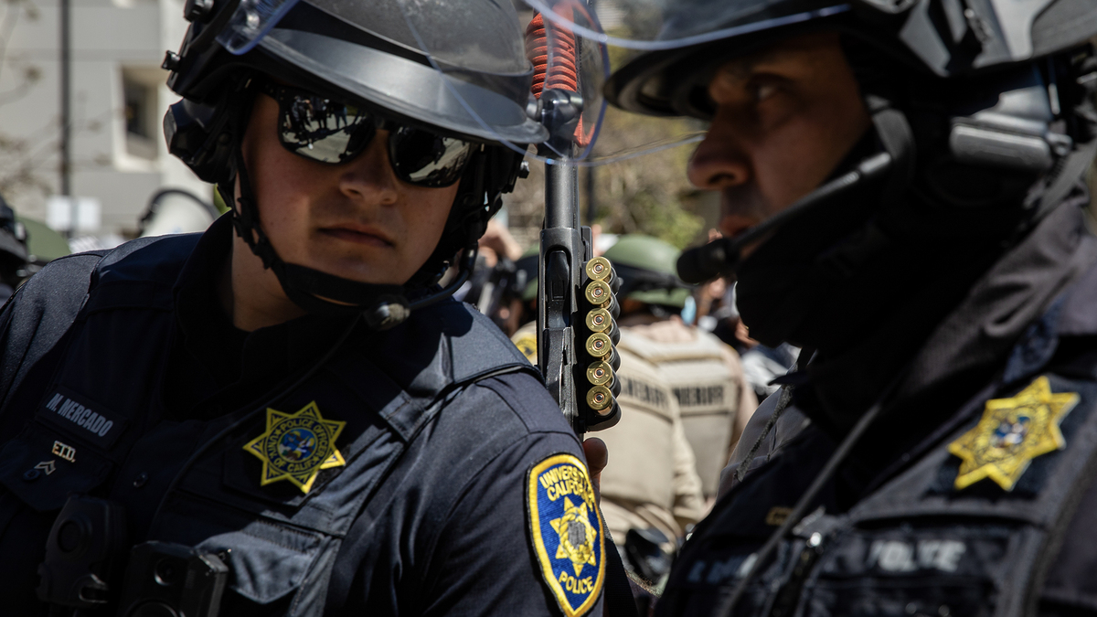 University of California campus police officers talk amongst each other while a San Diego Sheriff's officer holds a weapon behind them during a pro-Palestinian protest at UC San Diego in San Diego on May 6, 2024.