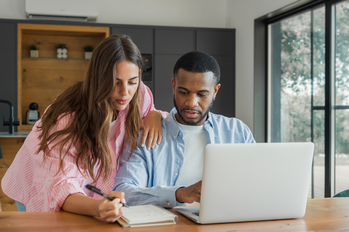  Stock photo of a couple sitting at a table looking at a laptop and notepad. 