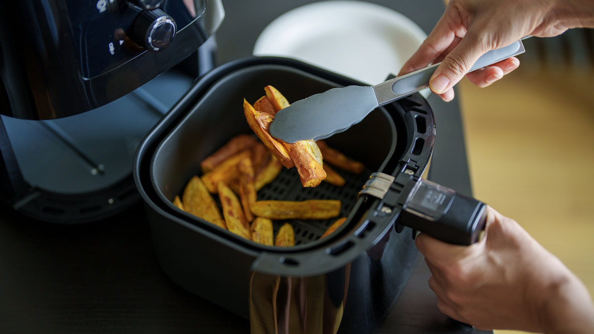 A woman is using an air fryer to prepare food in her kitchen, focusing on a healthier cooking method with minimal oil.