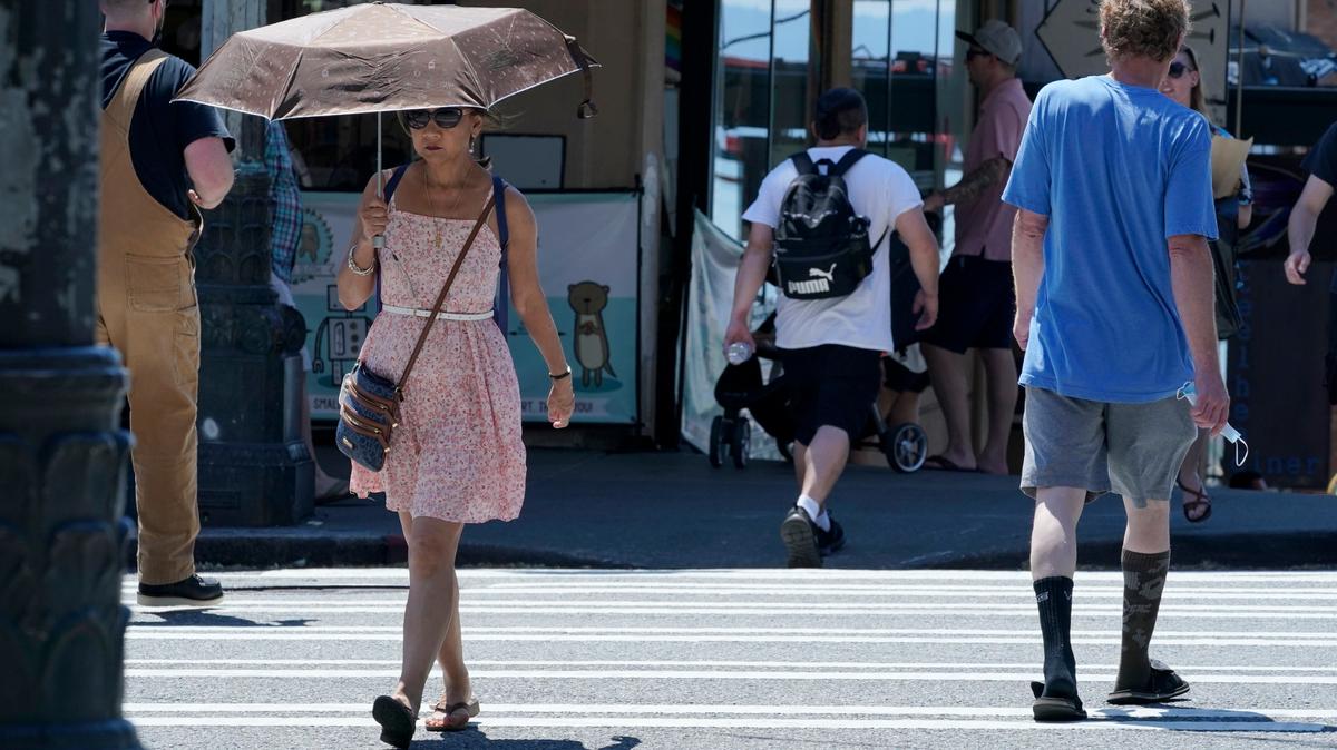Una mujer usa una sombrilla para protegerse del calor mientras camina en el Mercado Pike Place, el martes 29 de junio de 2021 en Seattle. La ola de calor sin precedentes en el noroeste de Estados Unidos que ha golpeado a Seattle y Portland, Oregon, ha afectado el suministro de electricidad en otras ciudades debido a la alta demanda de energía eléctrica.