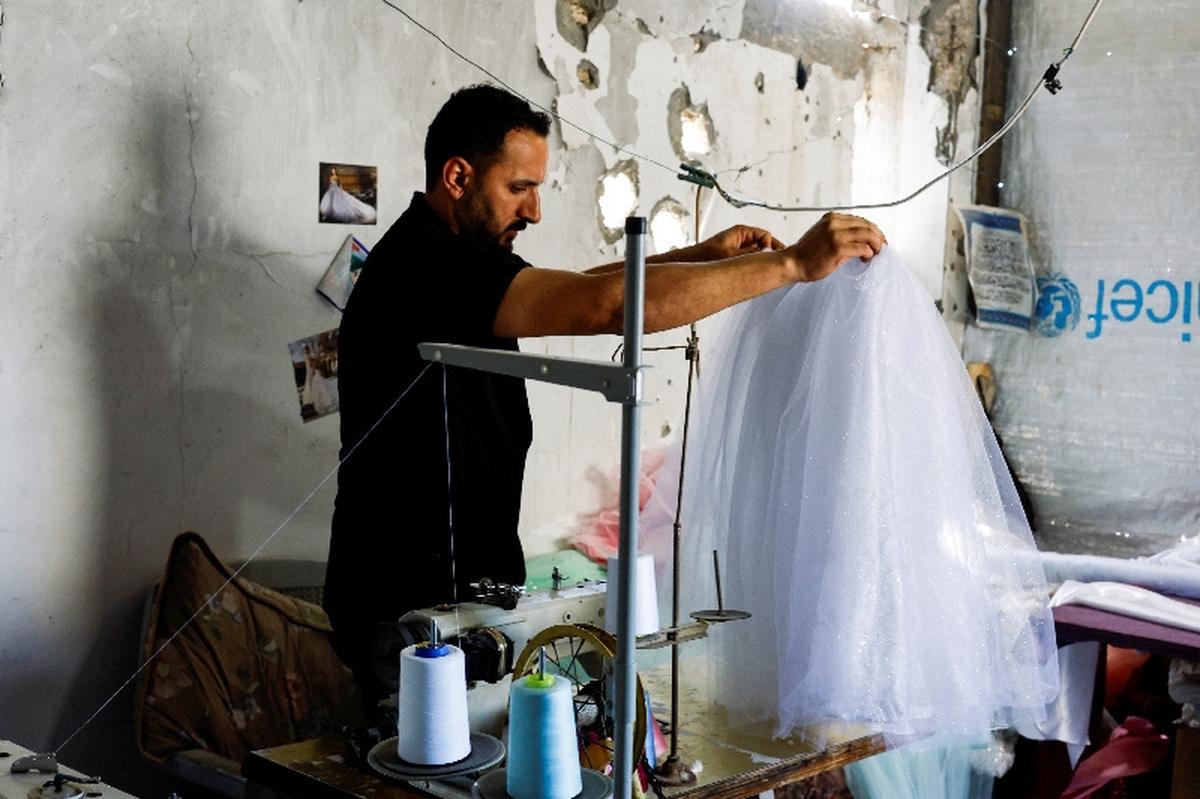 A Palestinian tailor repairs and recycles wedding dresses and children’s gowns at a shop with damaged walls, as families in Gaza turn to reused garments amid soaring prices and shortages caused by the war, in Khan Younis in the southern Gaza Strip, May 10, 2026. REUTERS/Mahmoud Issa