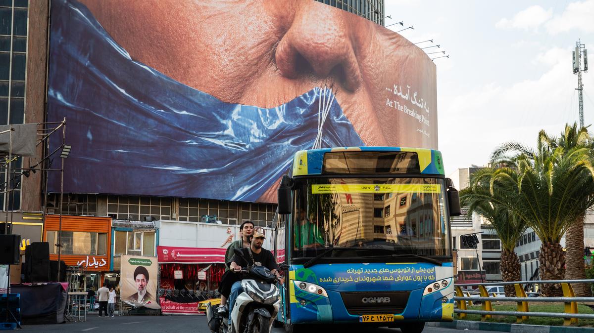People pass near a billboard showing the closure of the Strait of Hormuz over President Donald Trump's face with a message reading "At the Breaking Point" in Tehran, May 2, 2026. One key element of the proposed agreement between Iran and the United States is an apparent commitment by Tehran to give up its stockpile of highly enriched uranium, according to two U.S. officials. 