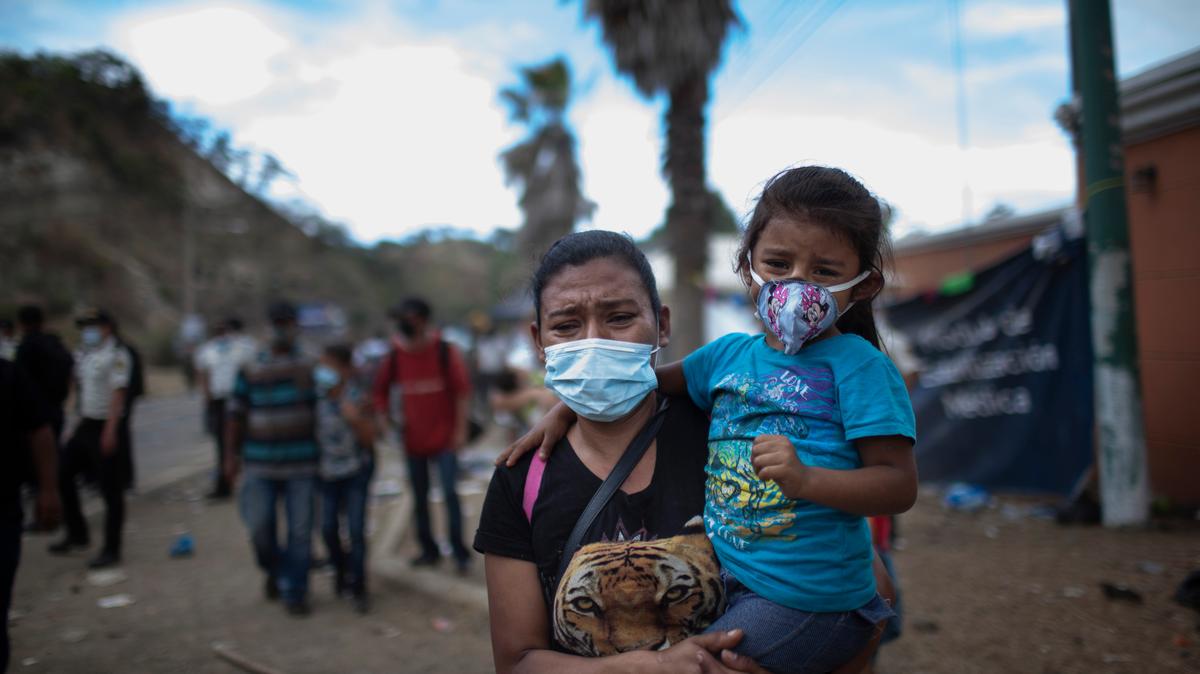 Una mujer con una niña en brazos se alejan mientras migrantes hondureños se enfrentan a soldados y policías guatemaltecos que les cortaban el paso en su avance hacia la frontera de Estados Unidos, en una carretera en Vado Hondo, Guatemala, el 18 de enero de 2021. El dispositivo se colocó estratégicamente en un cuello de botella de una vía de dos carriles franqueada por altas montañas y un muro, lo que dejó pocas opciones a los migrantes. (AP Foto/Sandra Sebastián)
