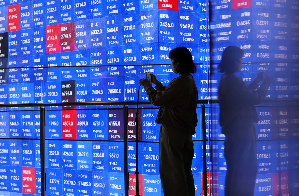 A visitor stands next to an electronic screen displaying Japan's Nikkei stock prices quotation board inside a conference hall in Tokyo, Japan March 4, 2026. REUTERS/Issei Kato