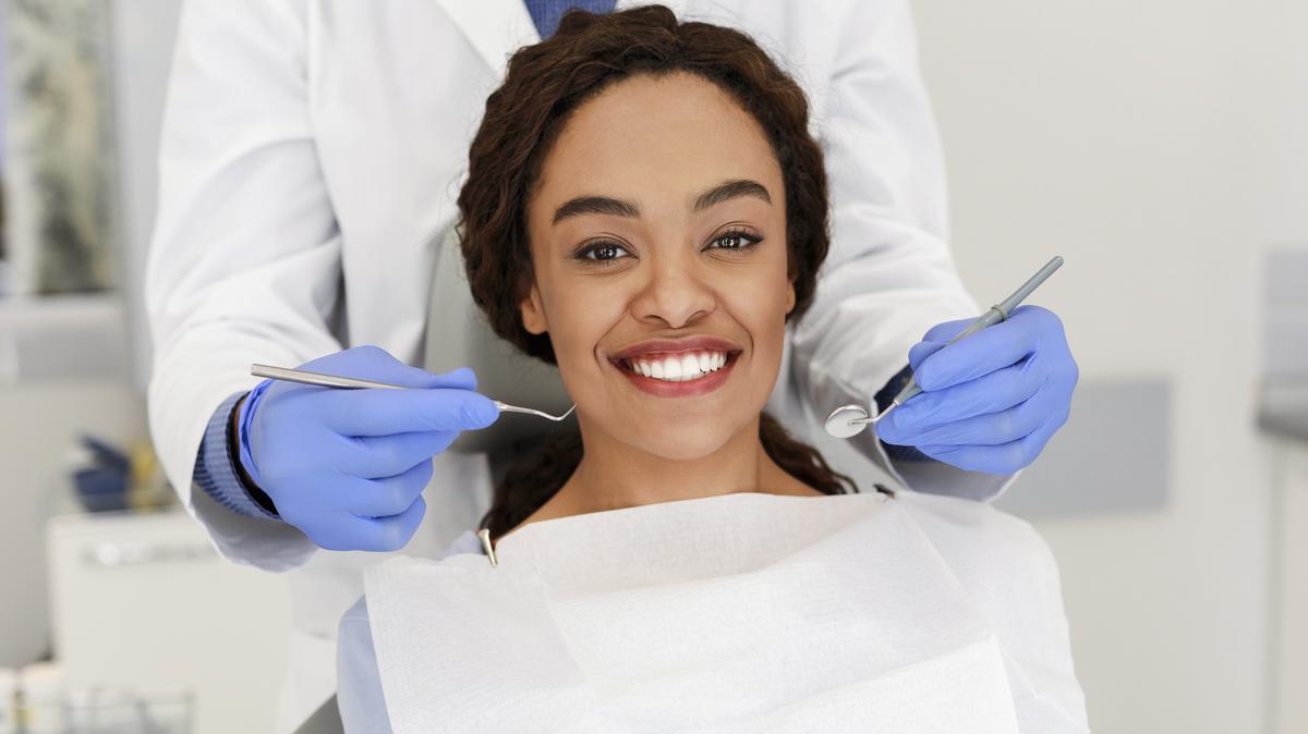 Cheerful african woman and hands of dentist staying behind
