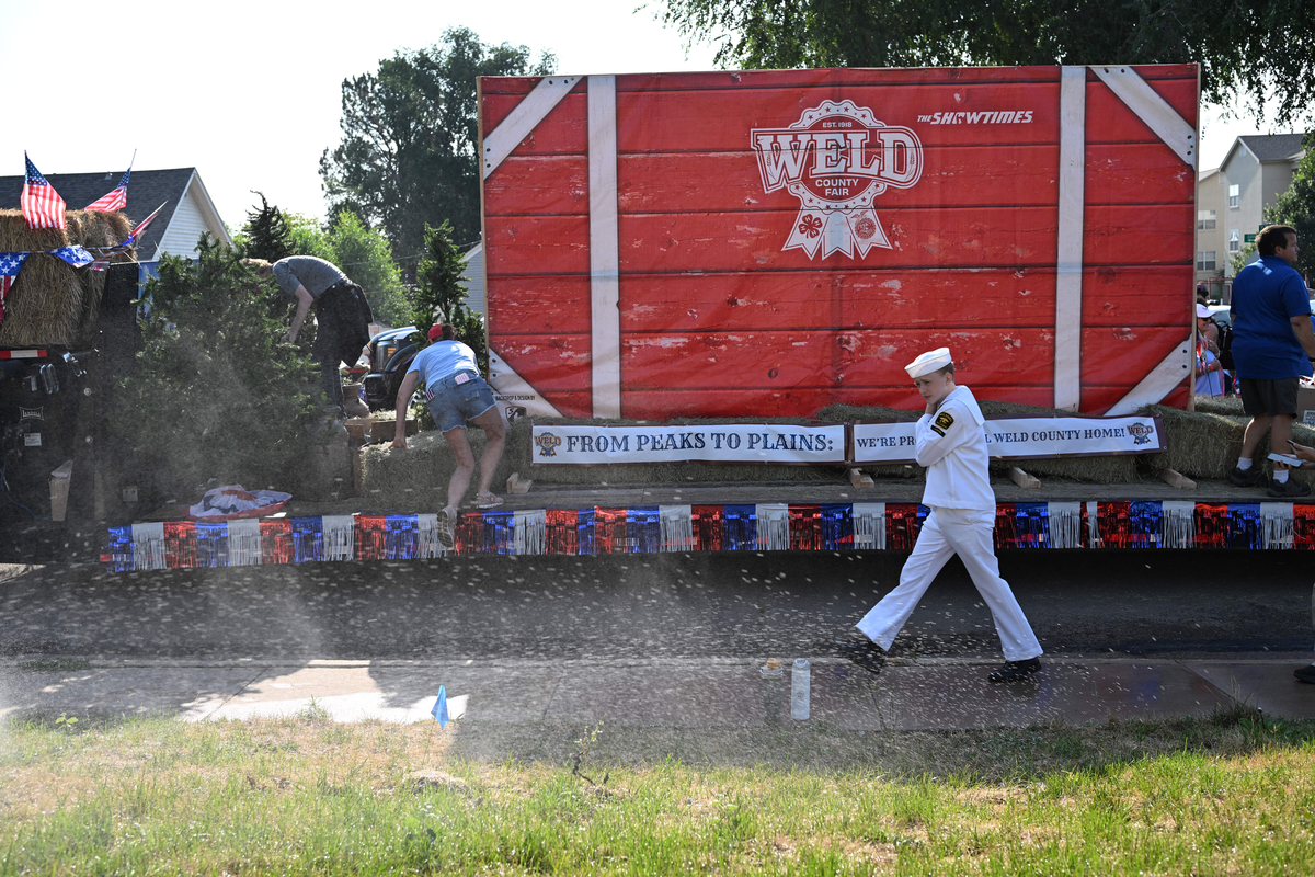 Participants walk past a house's front lawn sprinkler before the start of Greeley Stampede's Independence Day parade in Greeley, Colo., July 4, 2026. America celebrates the 250th anniversary of its independence today, with people from one end of the country to the other marking the milestone with fireworks, parades and concerts. (Mark Makela/The New York Times)