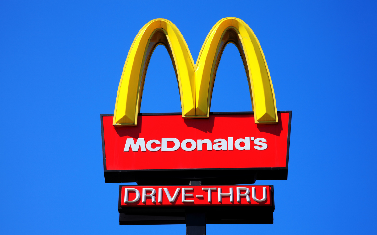  McDonald’s yellow and red drive-thru logo advertising sign placed on a pole with a clear blue sky 
