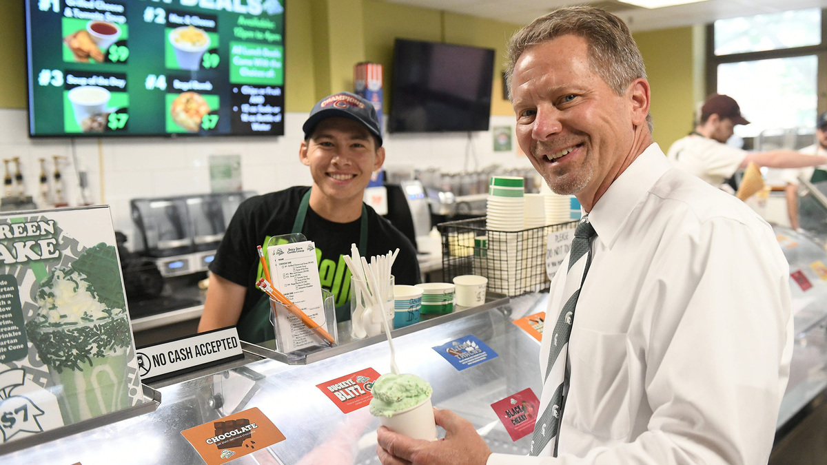 During a golf cart tour on campus, Michigan State University president Kevin Guskiewicz made the MSU Dairy Store one of the stops in East Lansing, Mich., on Sept. 18, 2024. From left, after serving the scoop of ice cream, Michigan State student Ben Adams, 22, of Arlington is photographed with Guskiewicz, holding a scoop of Presidential Gus-tachio, a pistachio ice cream has been named for Guskiewicz. (Robin Buckson/The Detroit News/TNS)