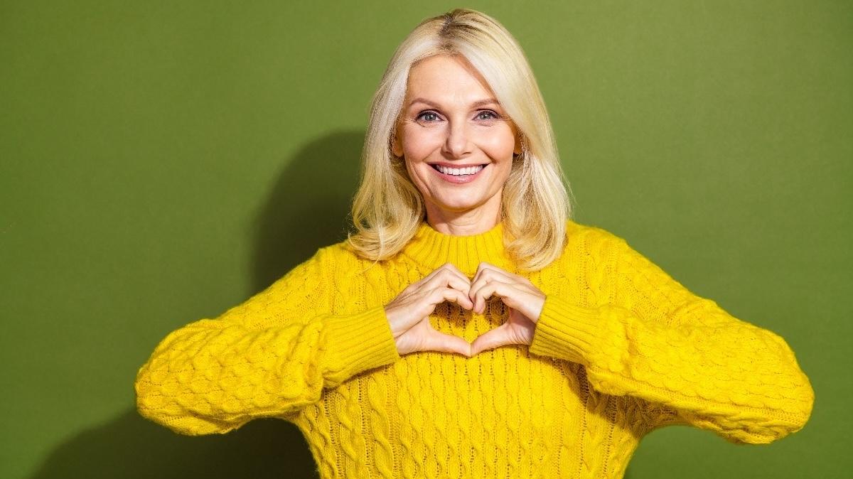 Portrait of nice aged woman show heart symbol wear yellow sweater isolated on khaki color background.