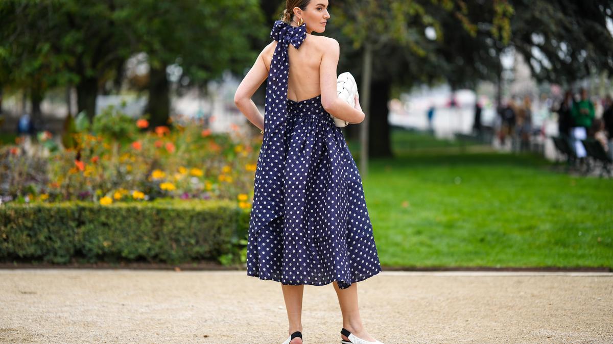 PARIS, FRANCE - OCTOBER 03: A guest wears gold earrings, a navy blue with white polka dots print pattern halter-neck / cut-out chest / midi dress, a white matte leather clutch from Bottega Veneta, white shiny leather pointed pumps heels shoes , outside Zimmermann, Paris Fashion Week - Womenswear Spring/Summer 2023, on October 03, 2022 in Paris, France. (Photo by Edward Berthelot/Getty Images)