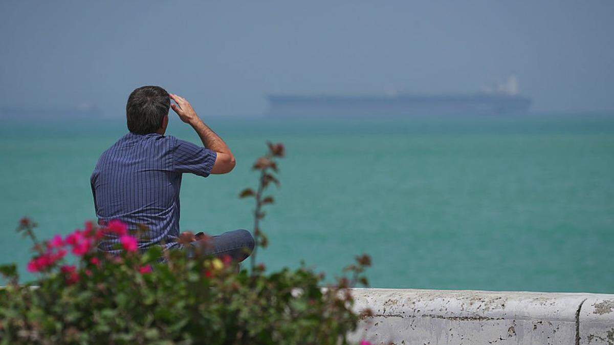 A man sits at the shoreline of Qeshm Island, Iran, as boats navigate the Strait of Hormuz on April 28. President Donald Trump said Sunday that the United States would launch a new effort to help guide stranded ships blockaded by both the U.S. and Iran out of the strait.