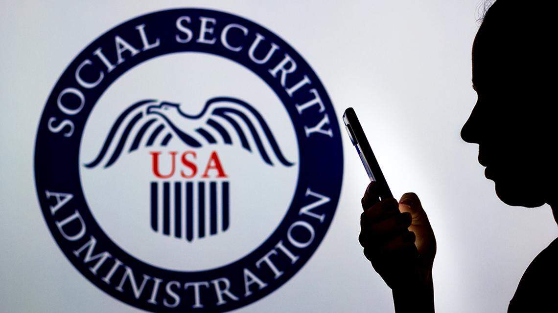 In this photo illustration, a woman’s silhouette holds a smartphone with the U.S. Social Security Administration logo in the background.