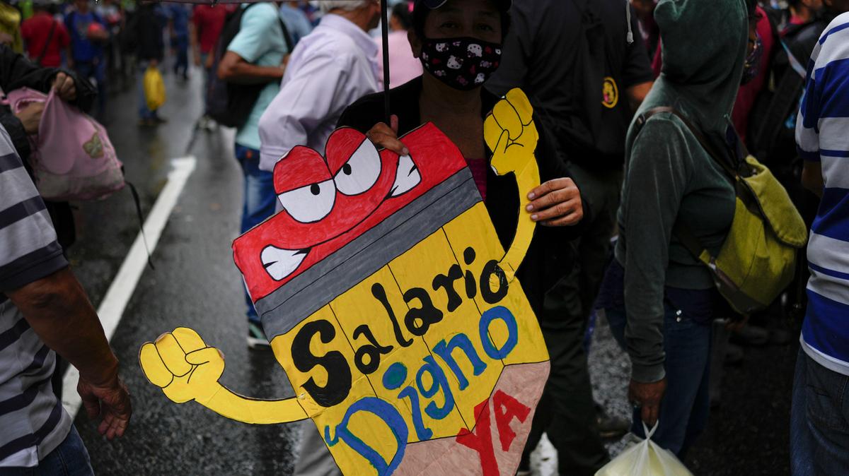 Un maestro sostiene un cartel durante una protesta de trabajadores públicos exigiendo que el gobierno pague sus beneficios completos y respete los convenios colectivos en Caracas, Venezuela, el miércoles 10 de agosto de 2022. (AP Foto/Matias Delacroix)