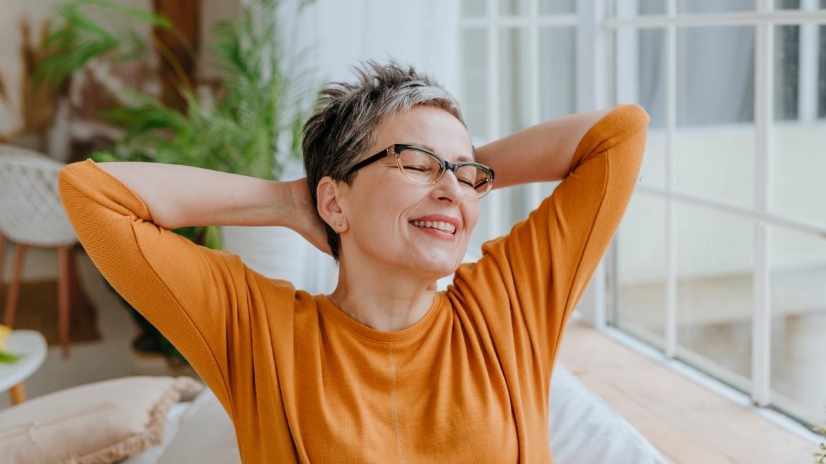 Happy woman with eyes closed and hands behind head at home