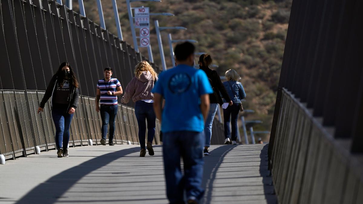 Unas personas caminan en un puente en el Puerto de Entrada de San Ysidro, que conecta la ciudad mexicana de Tijuana con Estados Unidos, el miércoles 13 de octubre de 2021, en San Diego. (AP Foto/Gregory Bull)