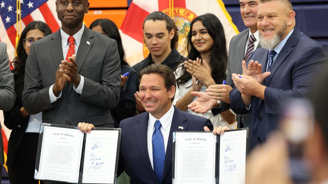 Florida Gov. Ron DeSantis holds up two signed house bills, including one allowing volunteer chaplains and religious leaders in schools as resources for students. (Rich Pope/Orlando Sentinel/TNS)