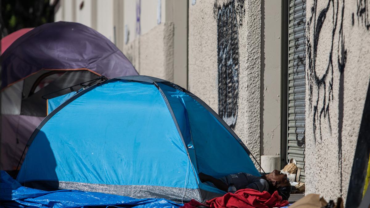 A homeless person lies in their tent on the sidewalk in front of the non-profit Midnight Mission's headquarters in the Skid Row neighborhood of downtown Los Angeles on Nov. 25, 2021. (Apu Gomes/AFP/Getty Images/TNS)
