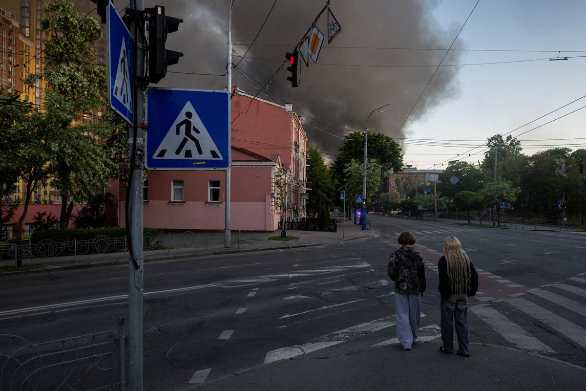 People walk on a street near a column of smoke rising from a building set ablaze during an overnight Russian missile and drone strike, amid Russia's attack on Ukraine, in Kyiv, Ukraine, May 24, 2026. REUTERS/Thomas Peter