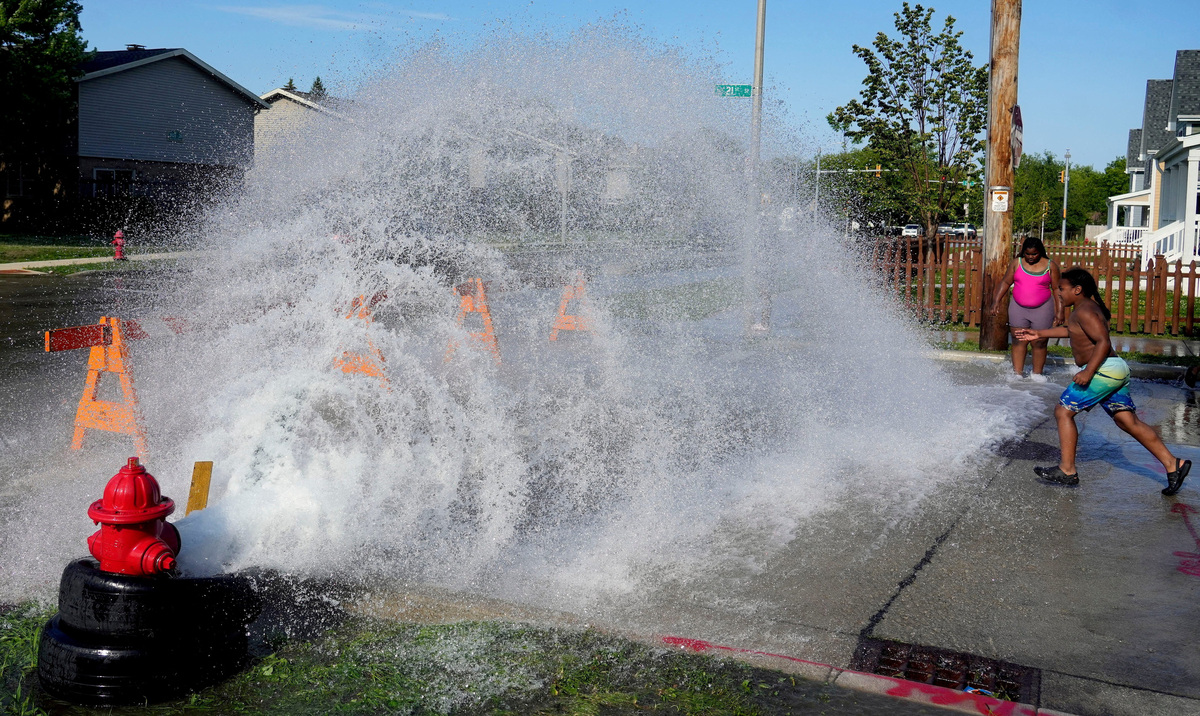 An unauthorized fire hydrant opening offers temporary relief from extreme heat for children in Milwaukee on Monday.