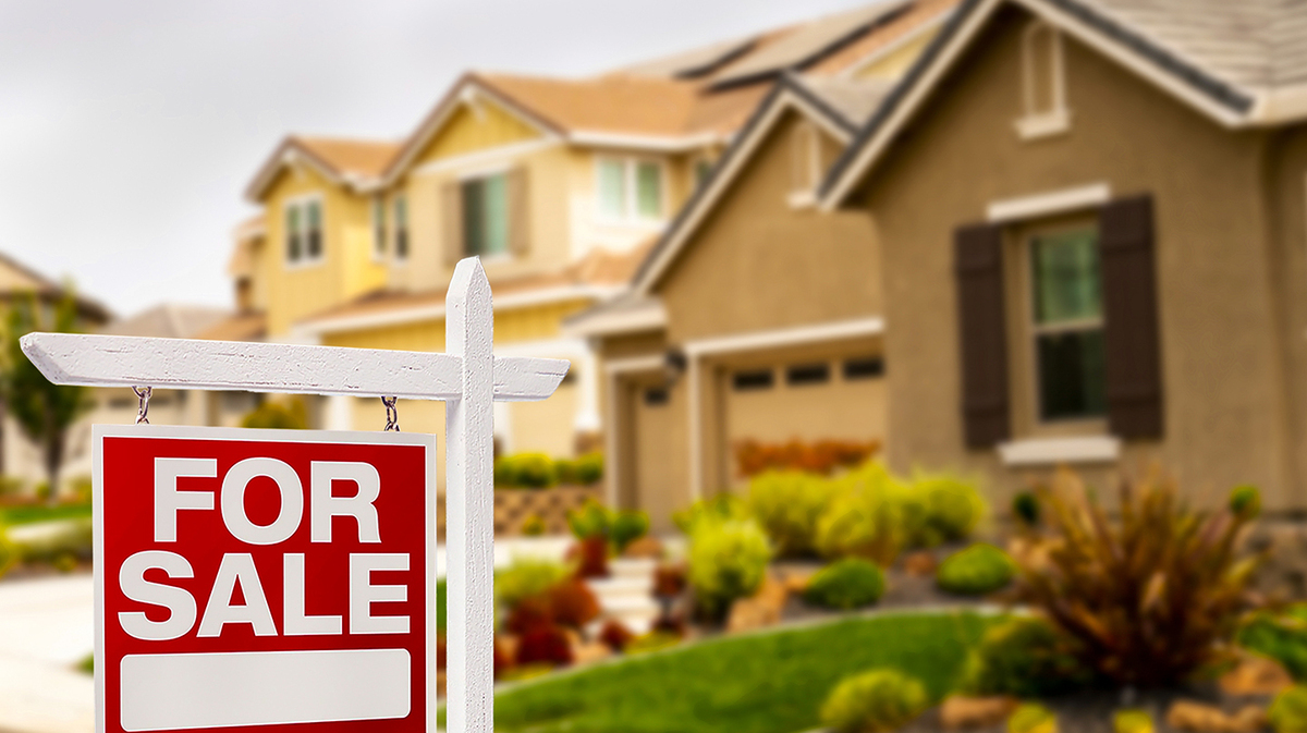 A photo of a house with a for sale sign in front.