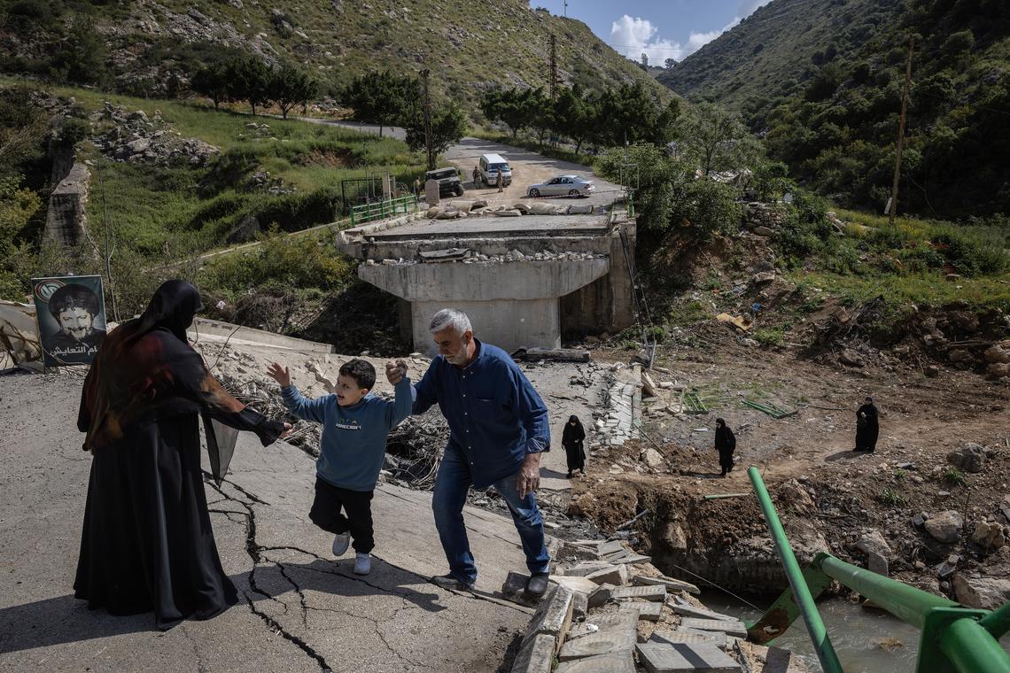 A boy is welcomed by his aunt and uncle on Monday, April 20, 2026, as he and his family, in the background, cross the wreckage of a bridge over the Litani River that was destroyed in an Israeli airstike near the village of Tayr Felsay, Lebanon. The boy and his family are among those displaced by the fighting who are returning to their homes in southern Lebanon as a cease-fire between Israel and Hezbollah appears to be largely holding. (David Guttenfelder/The New York Times)