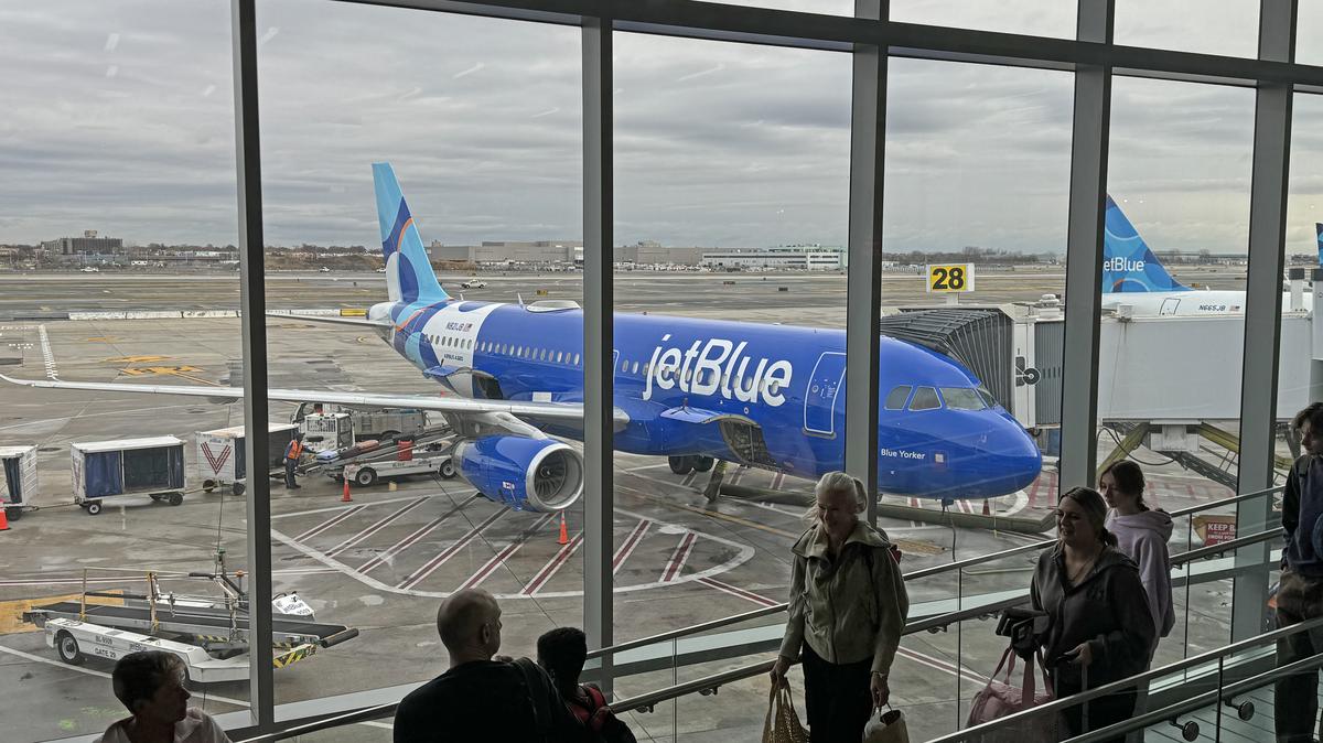 New York, 11/23/2024: Passengers line up for boarding a plane at JFK airport with a blue JetBlue aircraft in the background. 