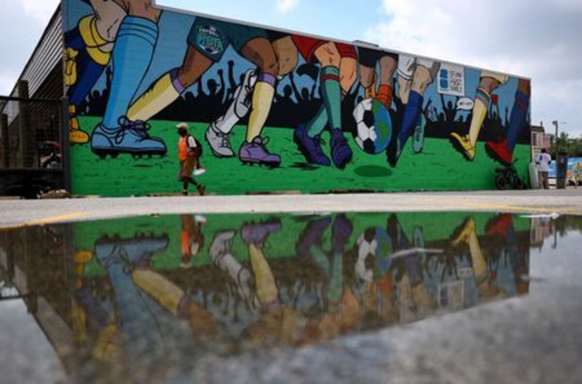 A parking attendent is reflected in a puddle in front of a World Cup-themed mural in Houston, Texas, U.S. June 18, 2026. REUTERS/Phil Noble