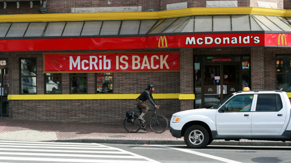 A man bicycles past a McDonald's restaurant on November 2, 2010 in Washington, featuring a sign announcing the return of the "McRib".