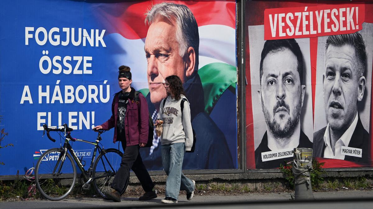A young couple walk in front of billboards, featuring Hungarian Prime Minister Viktor Orban (L) with a text, reading 'Come together against the war' as portrait of Ukraine's President Volodymyr Zelensky and Hungarian opposition leader Peter Magyar with the text reading, 'They are dangerous',(top) and 'Let's stop them, just Fidesz (governor party)(R)' are seen in Budapest's 11th district on April 10, 2026, two days before the elections. The "poster war" has entered an ever more intense phase in the run-up to the election campaign. Cities and roads are flooded with political advertisements. The elections will be held in Hungary on April 12. 