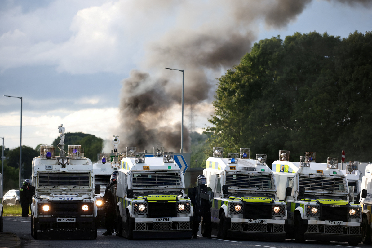 Smoke rises, as police stand by vehicles, as they control anti-immigrant protesters, following a knife attack on June 8, which left a man seriously injured and prompted police to declare a critical incident, in Belfast, Northern Ireland, June 10, 2026. REUTERS/Isabel Infantes