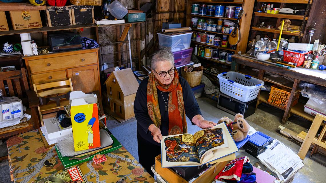 Leni Siegel, age 80, of Berkeley, pulls out a book while showing off the items she wants to get rid of while in her garage in Berkeley, Calif., on Thursday, April 16, 2026. Siegel, a senior citizen, is in the process of downsizing her home. (Jose Carlos Fajardo/Bay Area News Group)