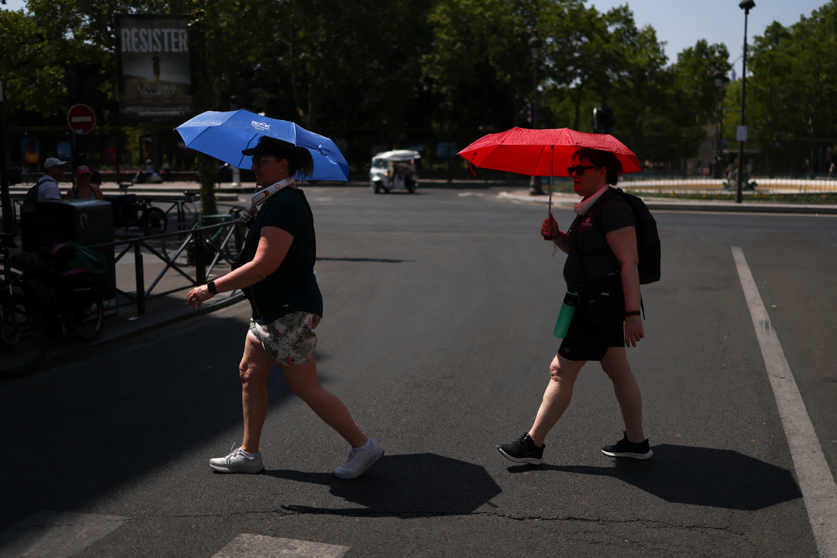 People cross the road whilst taking shelter under umbrellas in central Paris during high temperatures amid a heatwave in Paris, France, June 27, 2026. REUTERS/Tom Nicholson
