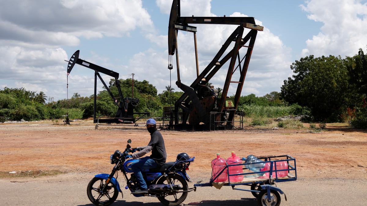 A man on a motorcycle transports water bottles past pumpjacks in Cabimas, Venezuela, January 26, 2026. REUTERS/Leonardo Fernandez Viloria