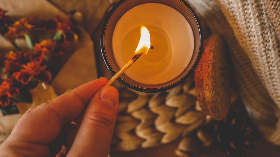Close-up of a hand lighting a red candle with a match, creating a warm and cozy atmosphere.