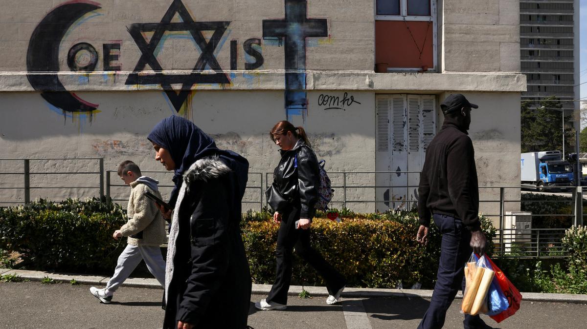 People walk past a mural which reads "coexist", made from religious symbols representing the religions of Islam, Judaism and Christianity, near to the market in the Paris suburb of Sarcelles, France, April 14, 2026. REUTERS/Tom Nicholson