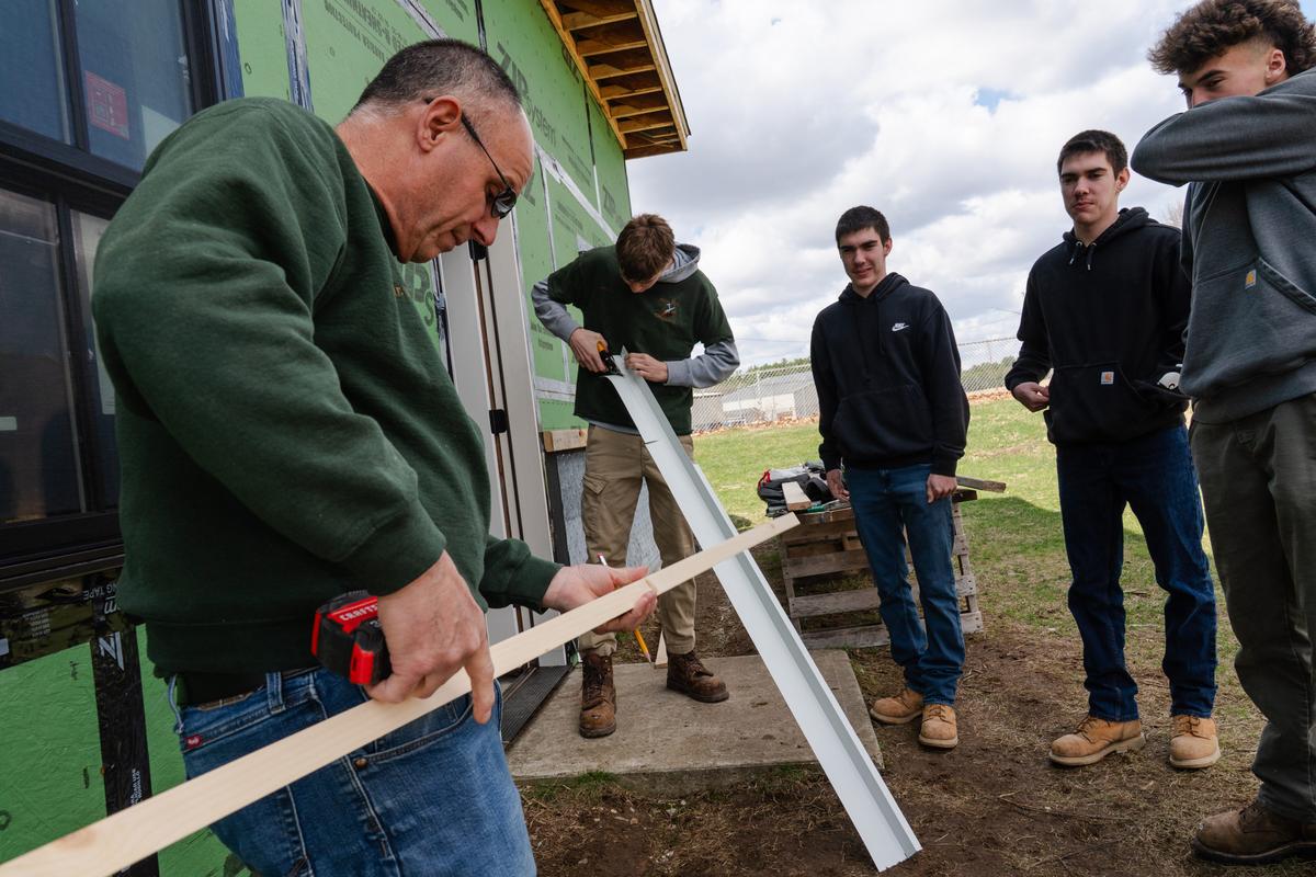  James Gallow, (left) the head of the carpentry department at Harvard H. Ellis Technical School, works with students on the house the carpentry class is building in Danielson, CT on April 7, 2026. Credit: Sophie Park for The Hechinger Report