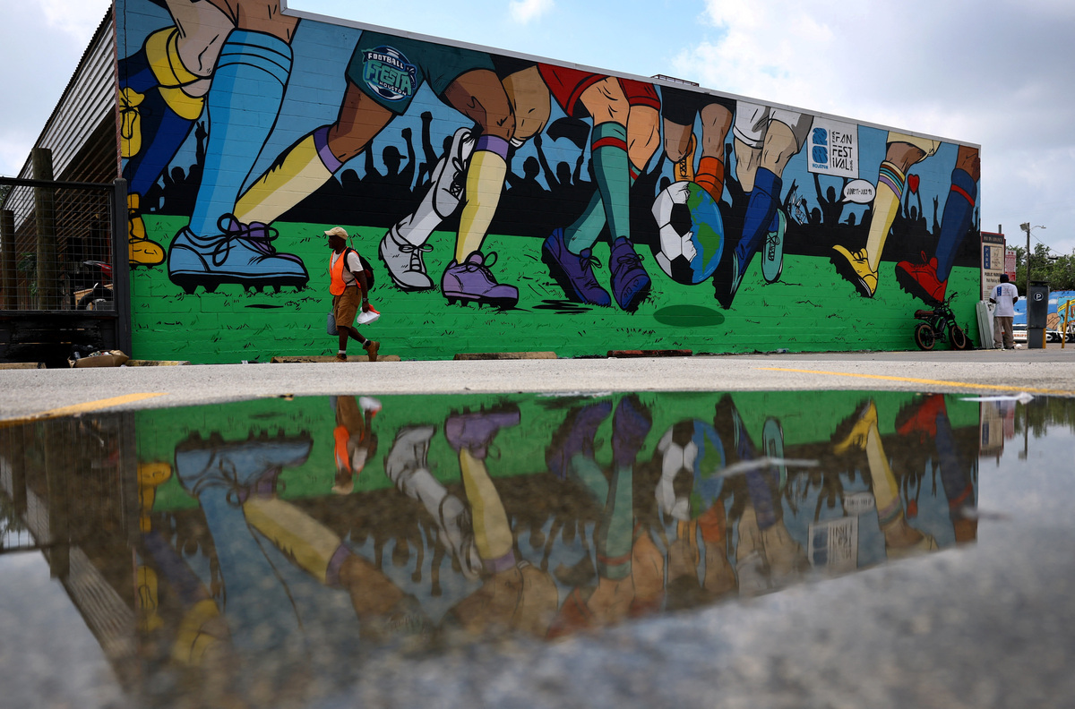 A parking attendent is reflected in a puddle in front of a World Cup-themed mural in Houston, Texas, U.S. June 18, 2026. REUTERS/Phil Noble