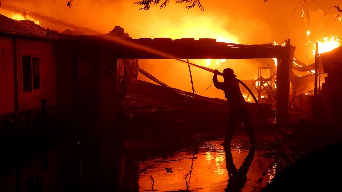 A firefighter sprays water on a burning home while battling the Eaton Fire on Jan. 8, 2025, in Altadena, California. AB 1383 in California proposes fair retirement age changes for firefighters, addressing toxic exposures, costs and preserving local collective bargaining.