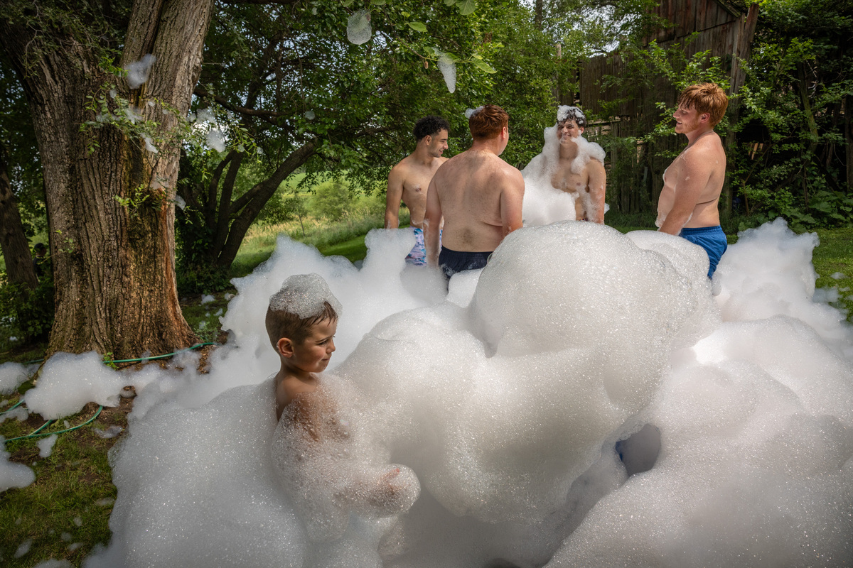 Fourth of July partyers play in bubbles at the top of a homemade waterslide, on a rural hillside in Adel, Iowa, on July 4, 2026. Though it was muggy and miserably hot in many parts of the country, the day was marked with the usual American exuberance, with fighter jets, tall ships, parachutists and flag-festooned pick-up trucks. (Kenny Holston/The New York Times)